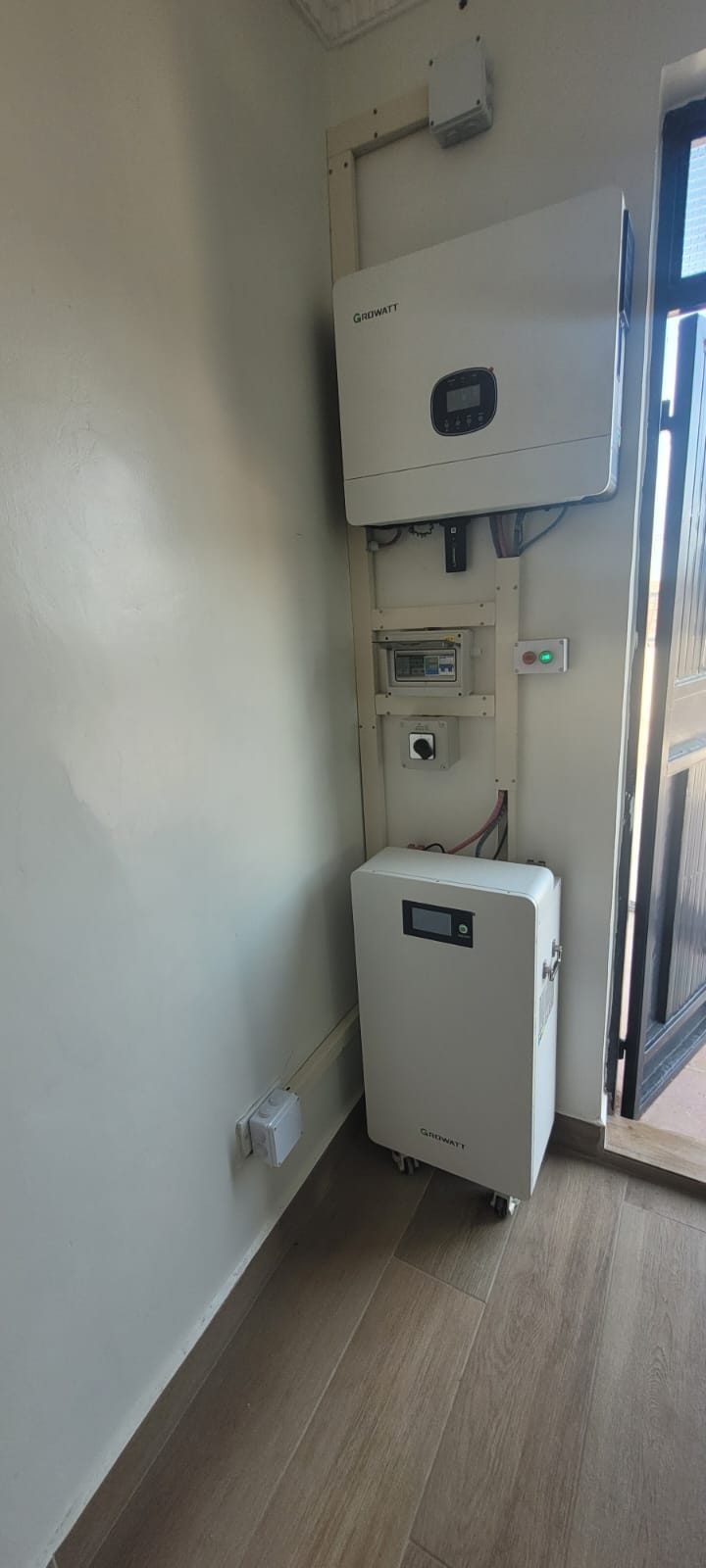 Wall-mounted Growatt hybrid inverter above a distribution box and a floor-standing Growatt battery